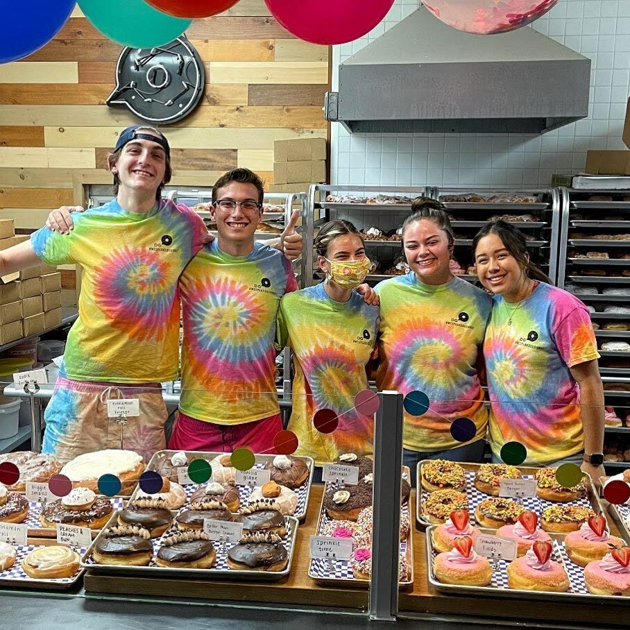 The Damn Good crew behind a full catering table of doughnuts at a community event